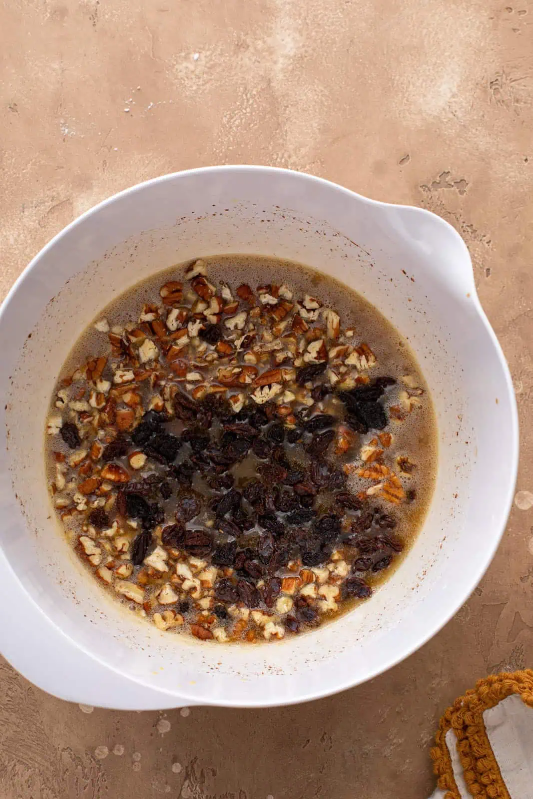 Chopped pecans and raisins being added to pecan pie filling in a bowl.