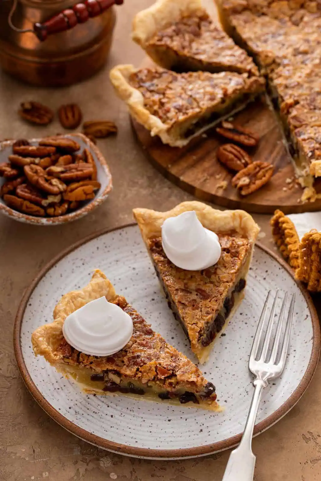 Two slices of pecan raisin pie, each topped with a dollop of whipped cream, on a plate.