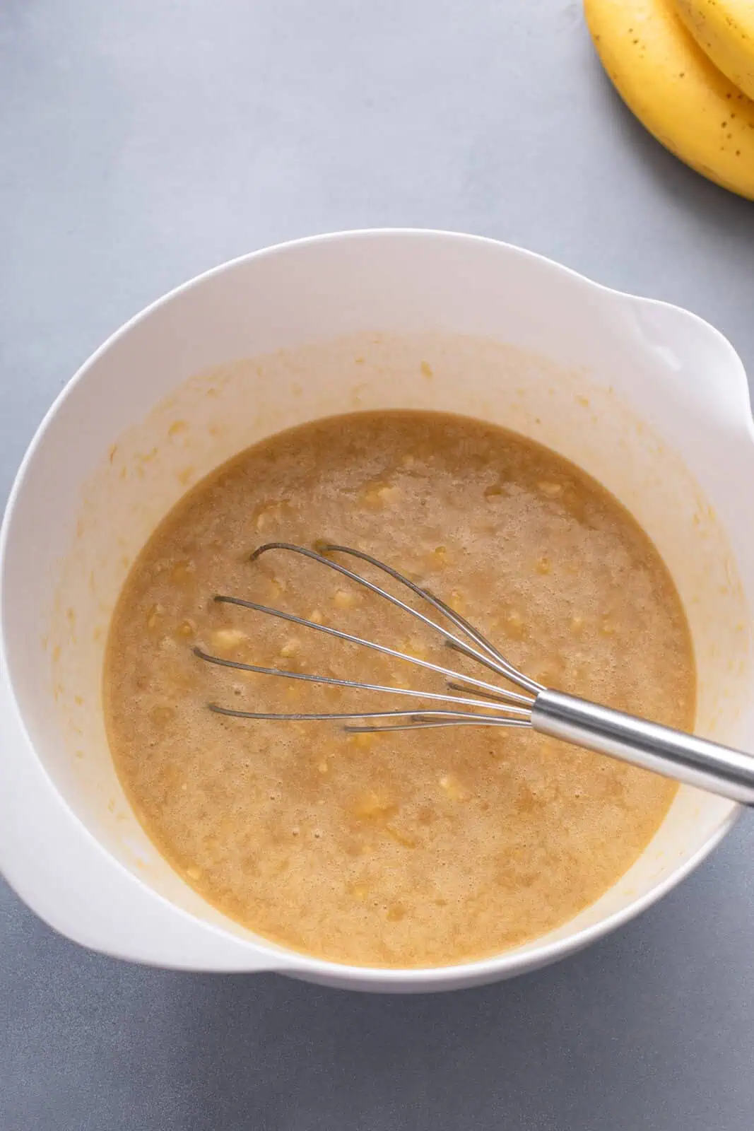 Wet ingredients for banana oat muffins whisked together in a white bowl.