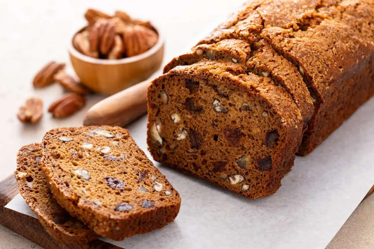 Sliced loaf of date nut bread set on a piece of parchment paper on a cutting board.