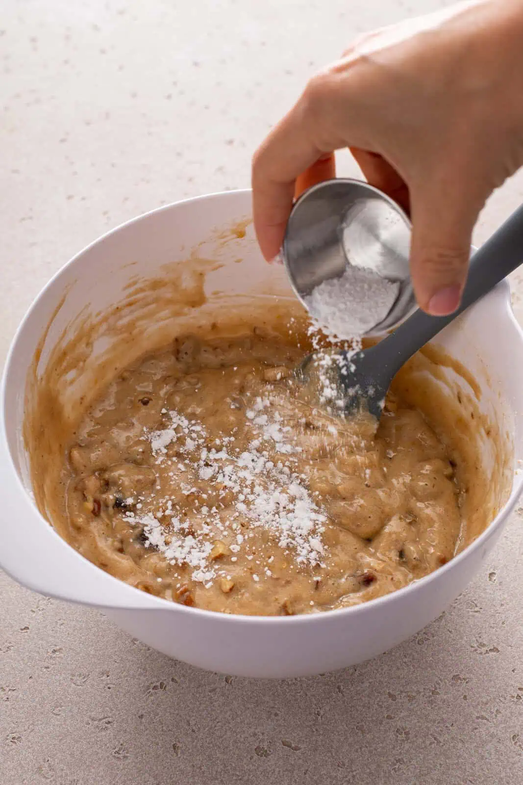 Hand sprinkling baking powder over date nut bread batter in a bowl.