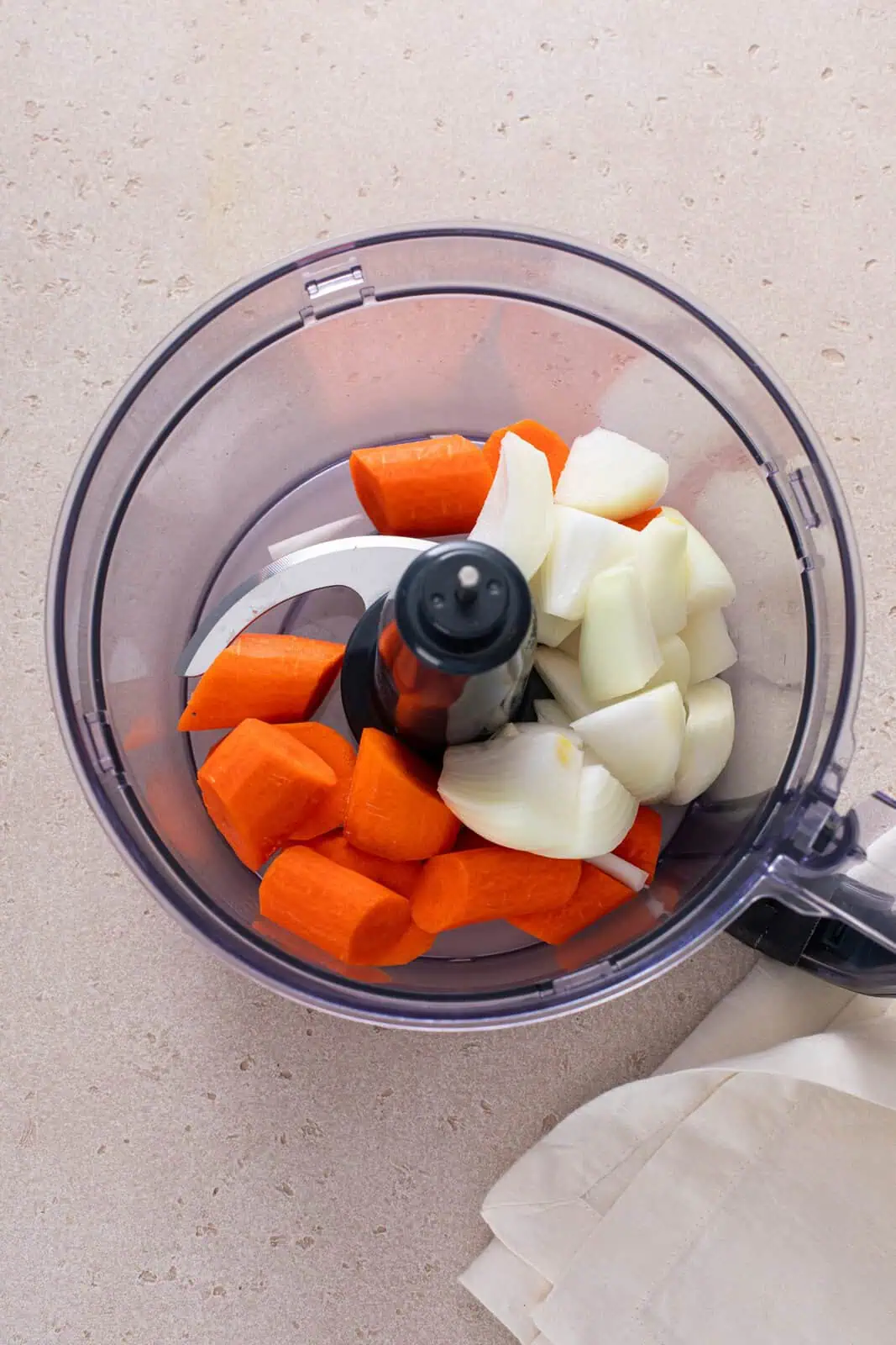 Carrots and onion cut into big chunks in the bowl of a food processor.