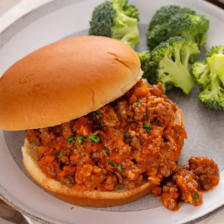 Sloppy joe sandwich next to broccoli on a white plate.