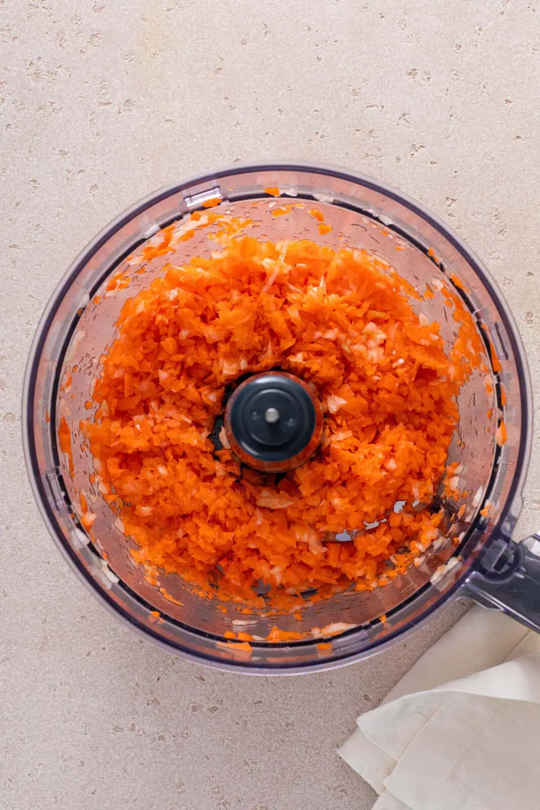 Carrots and onion cut into big chunks in the bowl of a food processor.