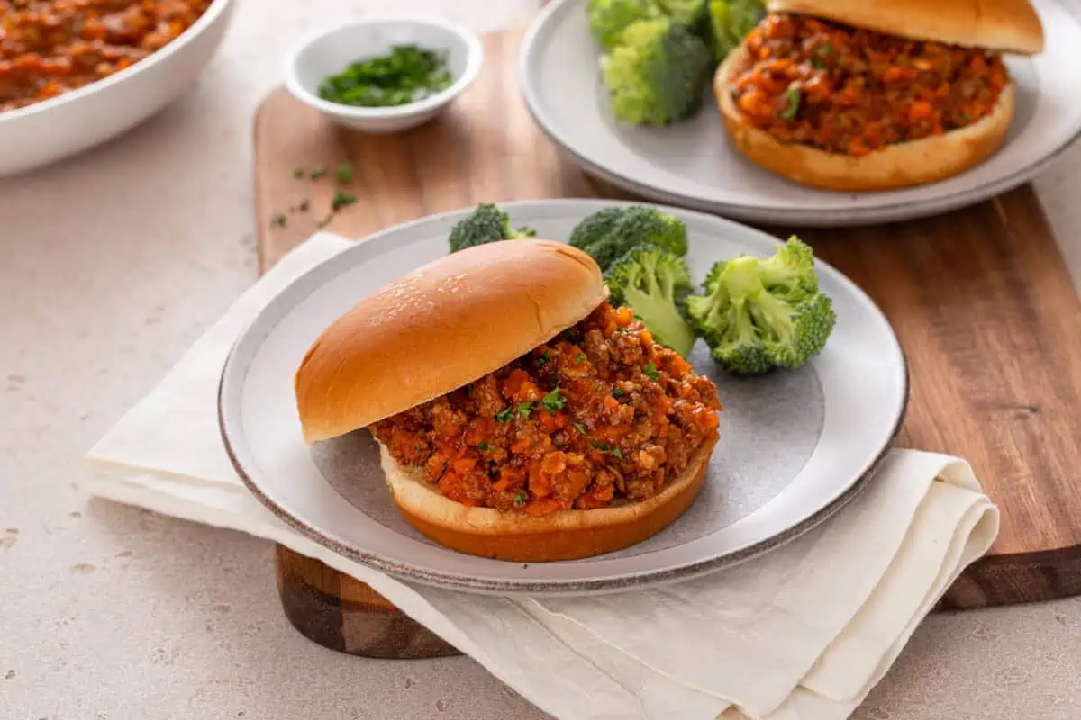 Plated sloppy joe sandwich and broccoli on a wooden board.