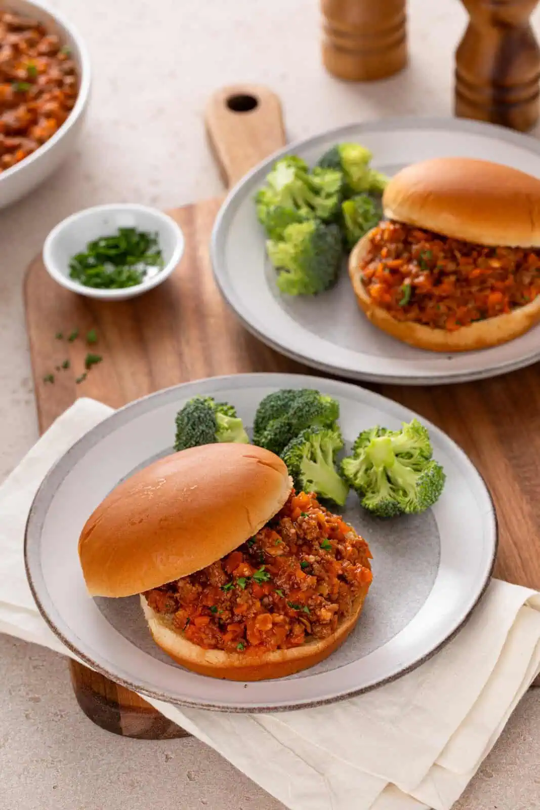 Two plates each holding a sloppy joe sandwich and broccoli.