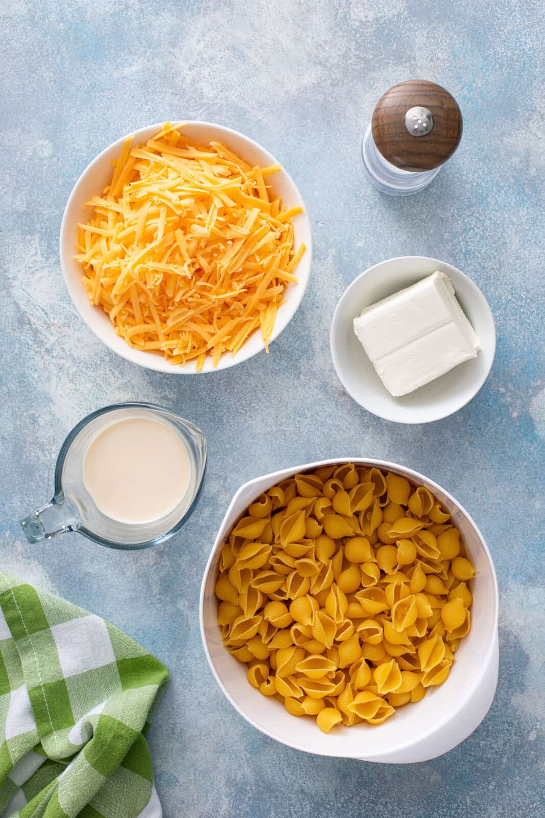 Ingredients for homemade shells and cheese arranged on a blue countertop.