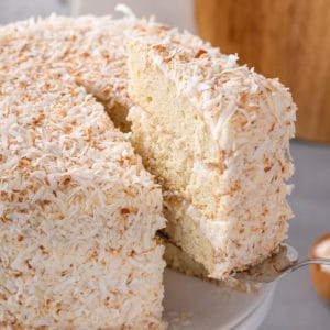 Slice of coconut cake being lifted from the whole cake.