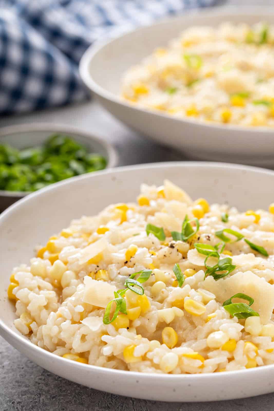 Close up of sweet corn risotto topped with green onion in a white bowl.