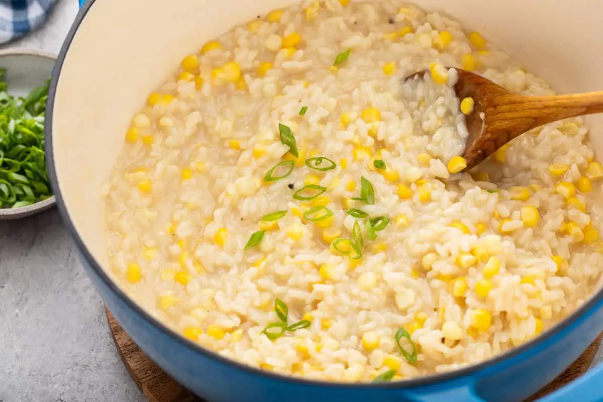 Close up of sweet corn risotto garnished with green onion in a dutch oven.