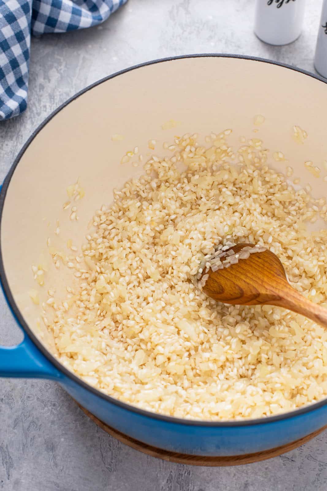 Sauteed onion and arborio rice being stirred in a dutch oven.