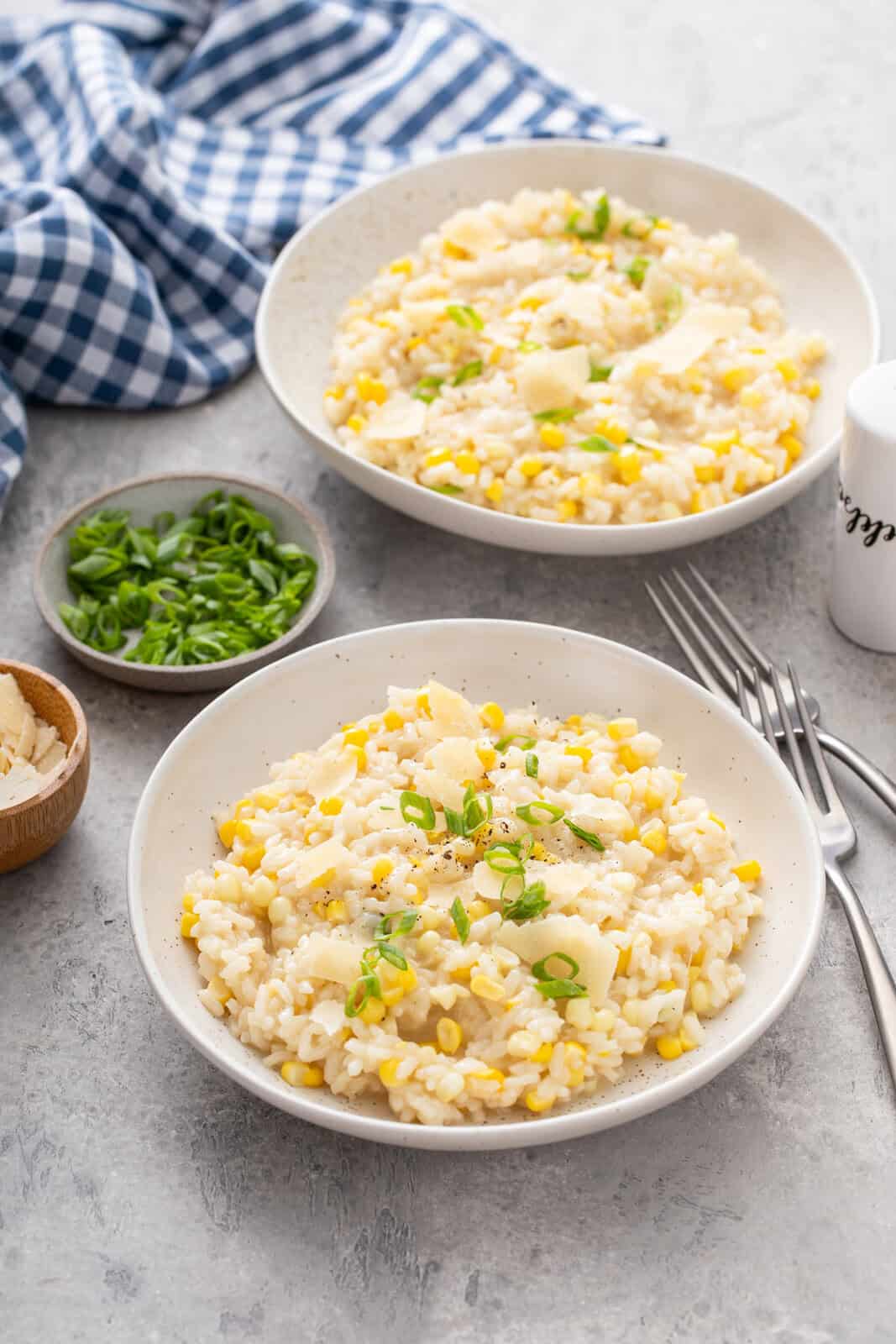 Two white bowls, each filled with sweet corn risotto and garnished with green onion.