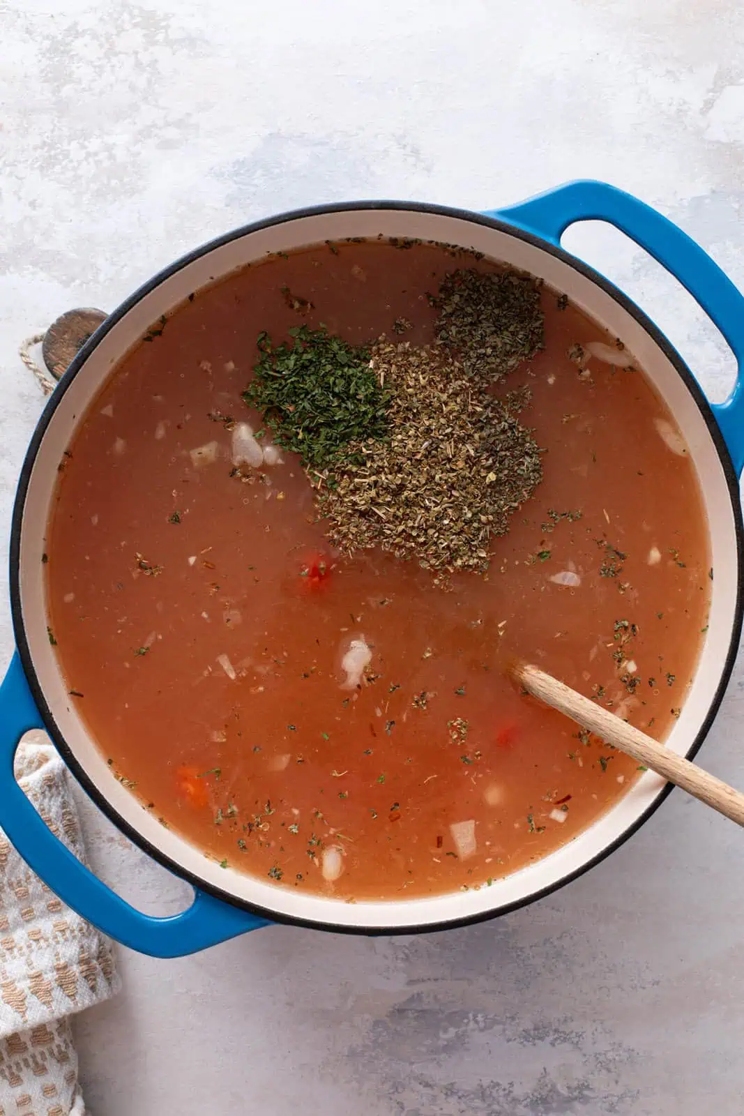 Stock, tomatoes, and herbs added to a dutch oven for tortellini soup.