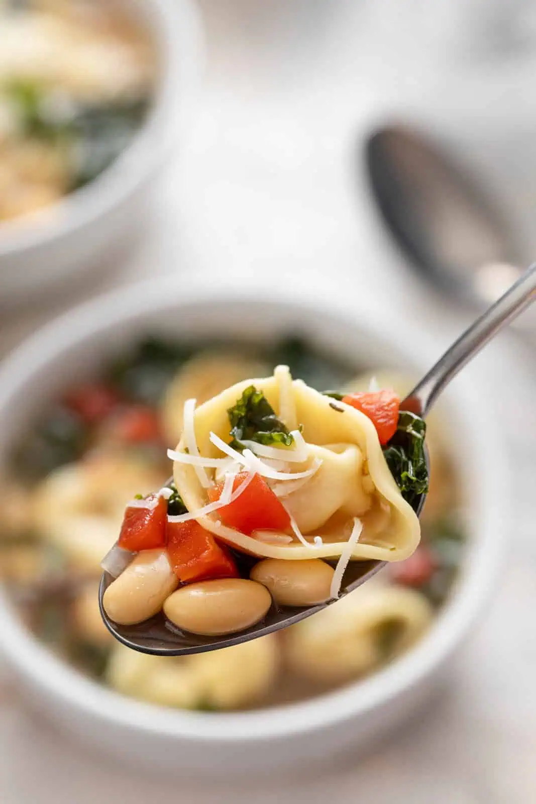 Spoon holding up a bite of easy tortellini soup.