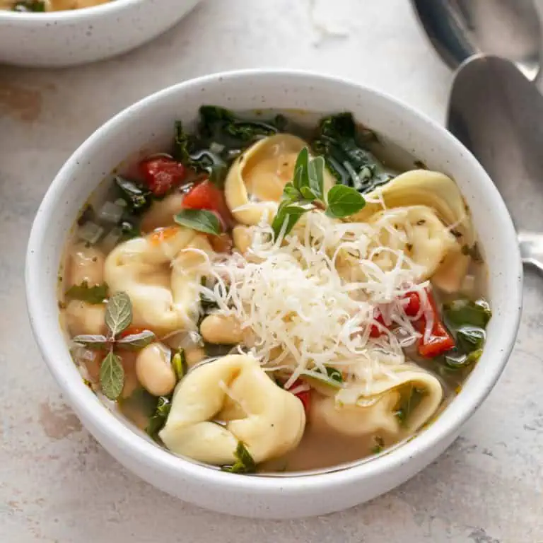 Close up of tortellini soup in a white bowl.