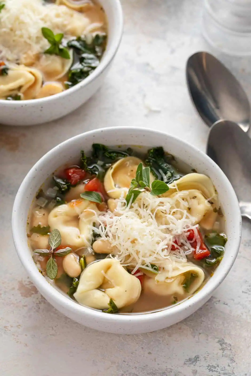 White bowl filled with easy tortellini soup topped with parmesan cheese.