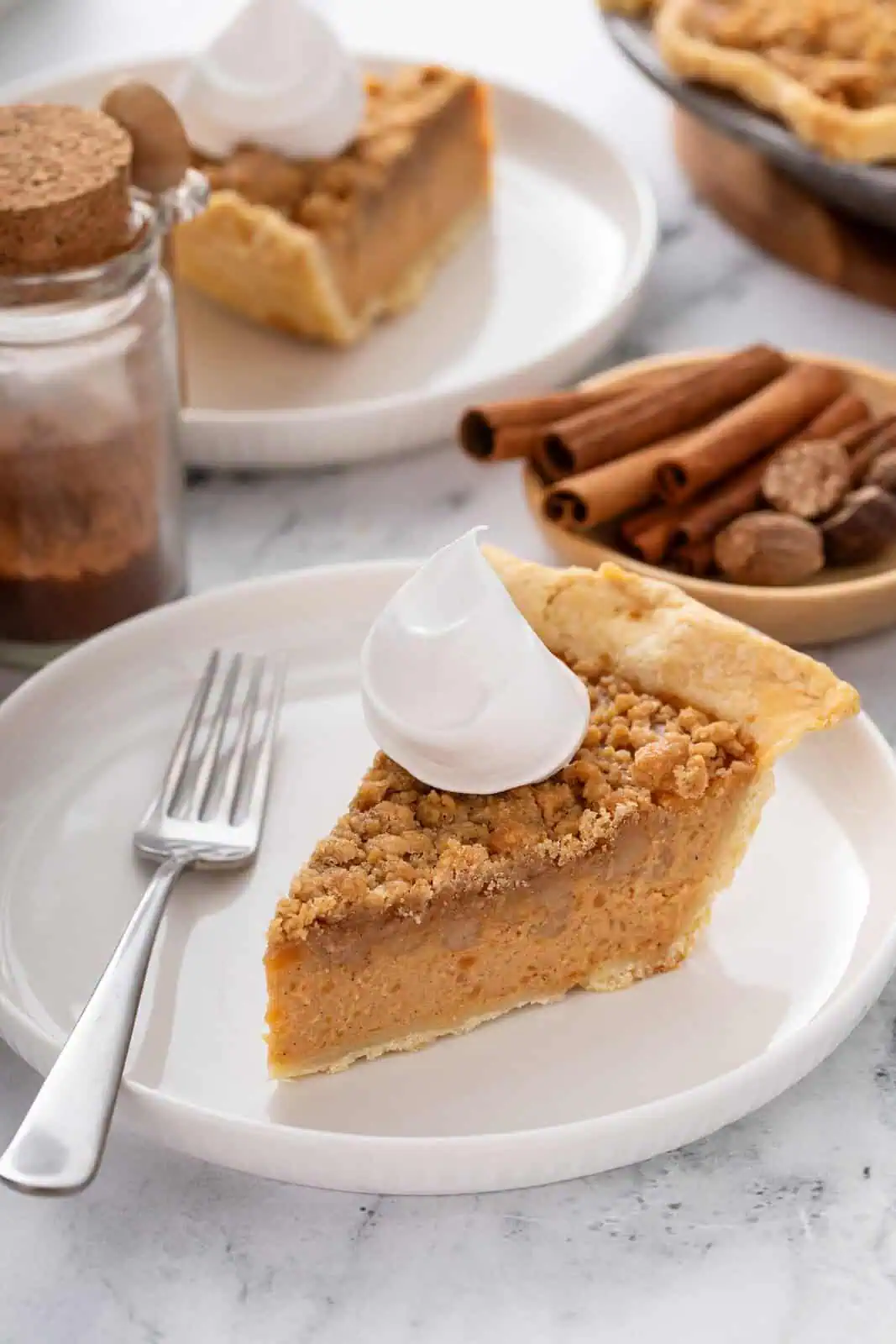 Slice of sweet potato pie on a white plate, topped with a dollop of whipped cream.