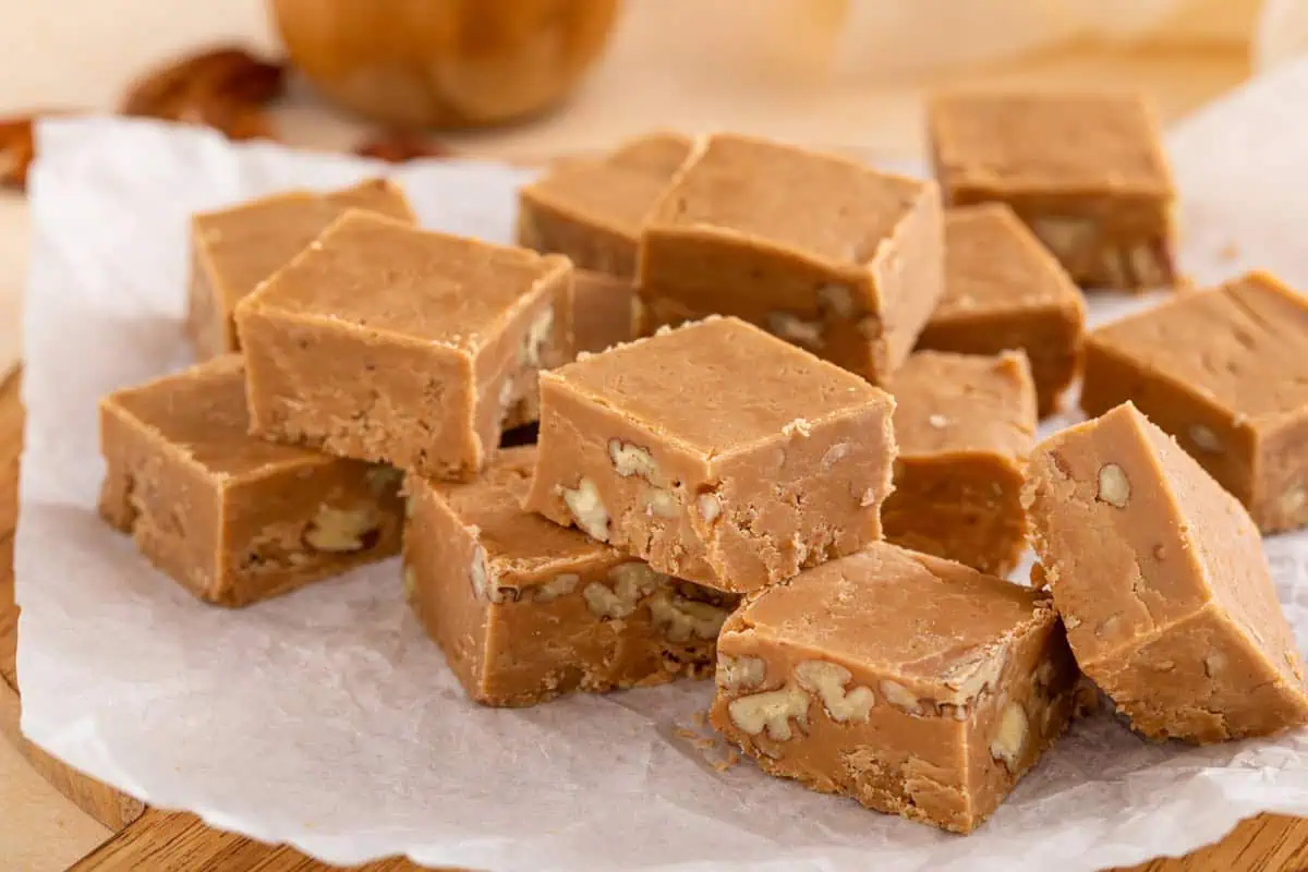 Brown sugar fudge pieces scattered and stacked on a piece of parchment paper.