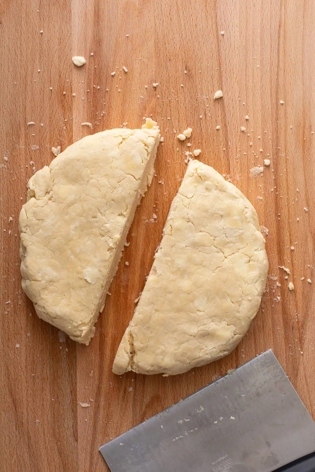 Disk of pie dough cut in half on a wooden board.