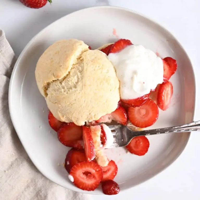 Fork taking a bite of strawberry shortcake on a white plate.