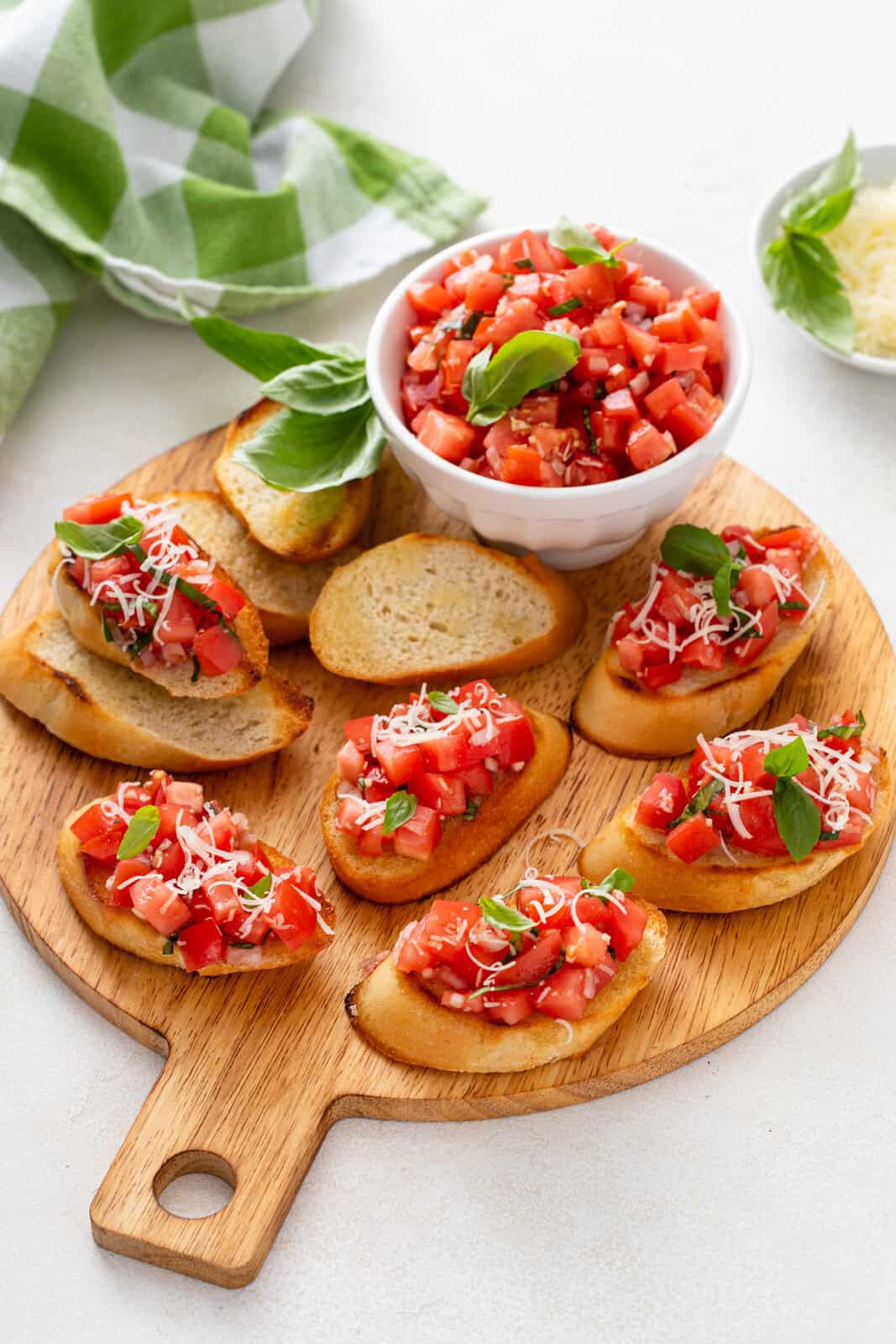 A bowl of tomato bruschetta topping next to slices of topped bruschetta on a wooden board.