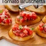 Olive oil being drizzled over tomato bruschetta on a wooden board. Text overlay includes recipe name.