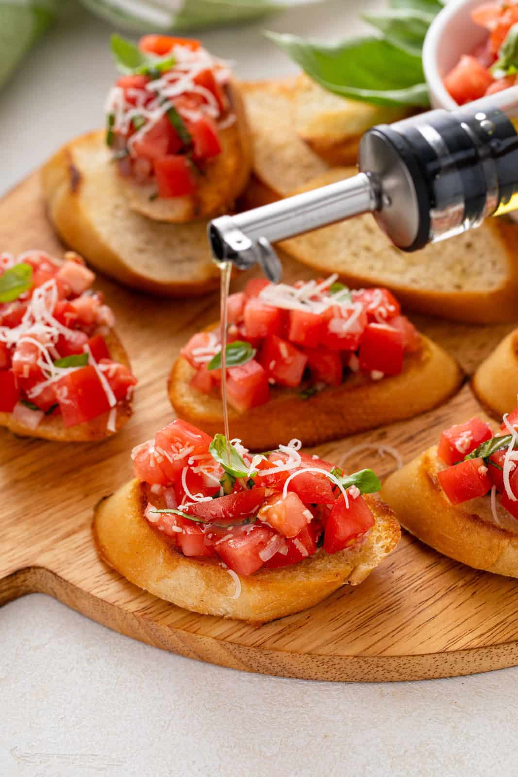 Olive oil being drizzled over tomato bruschetta on a wooden board.