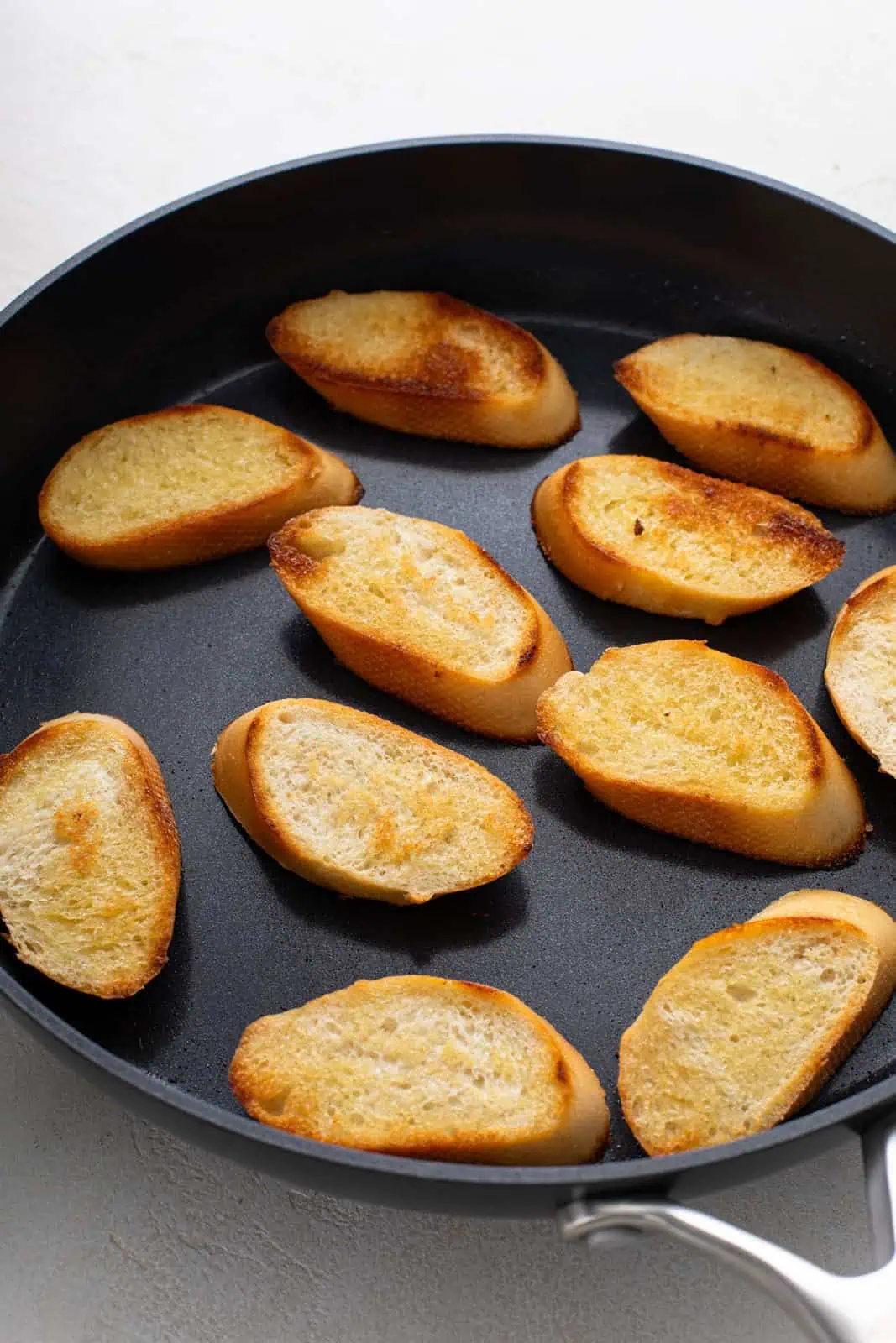 Toasted baguette slices in a black skillet.