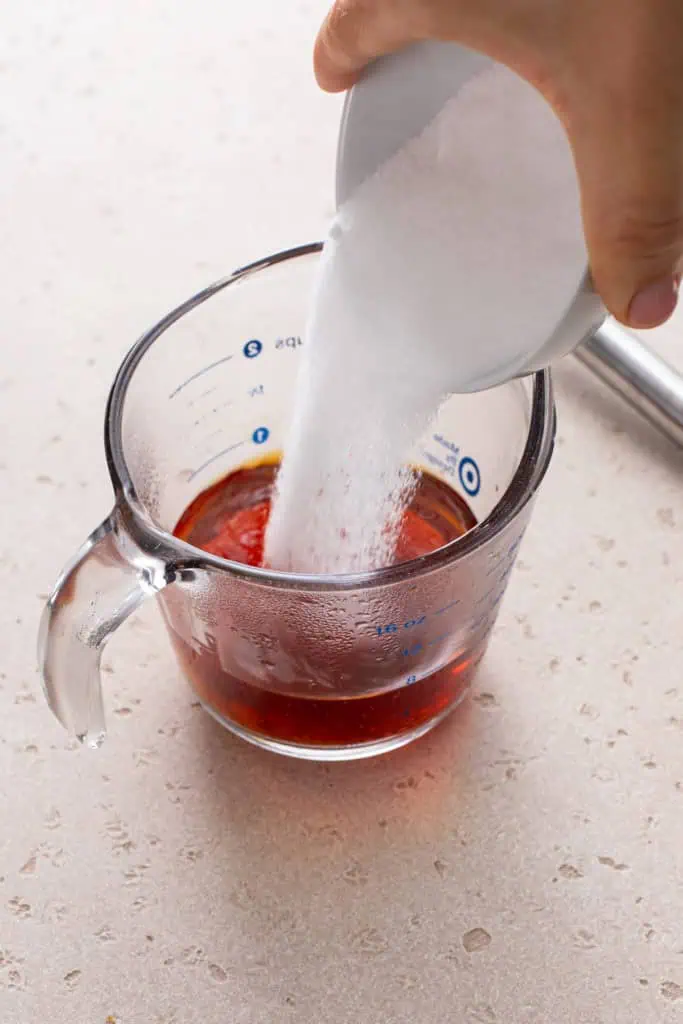 Sugar being poured into black tea in a measuring cup.