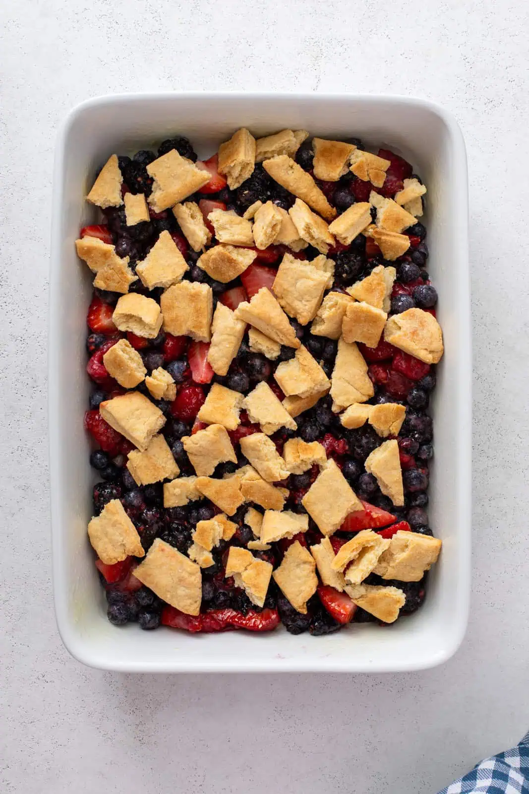 Layer of mixed berry cobbler filling in a baking dish, topped with pieces of baked pastry dough.