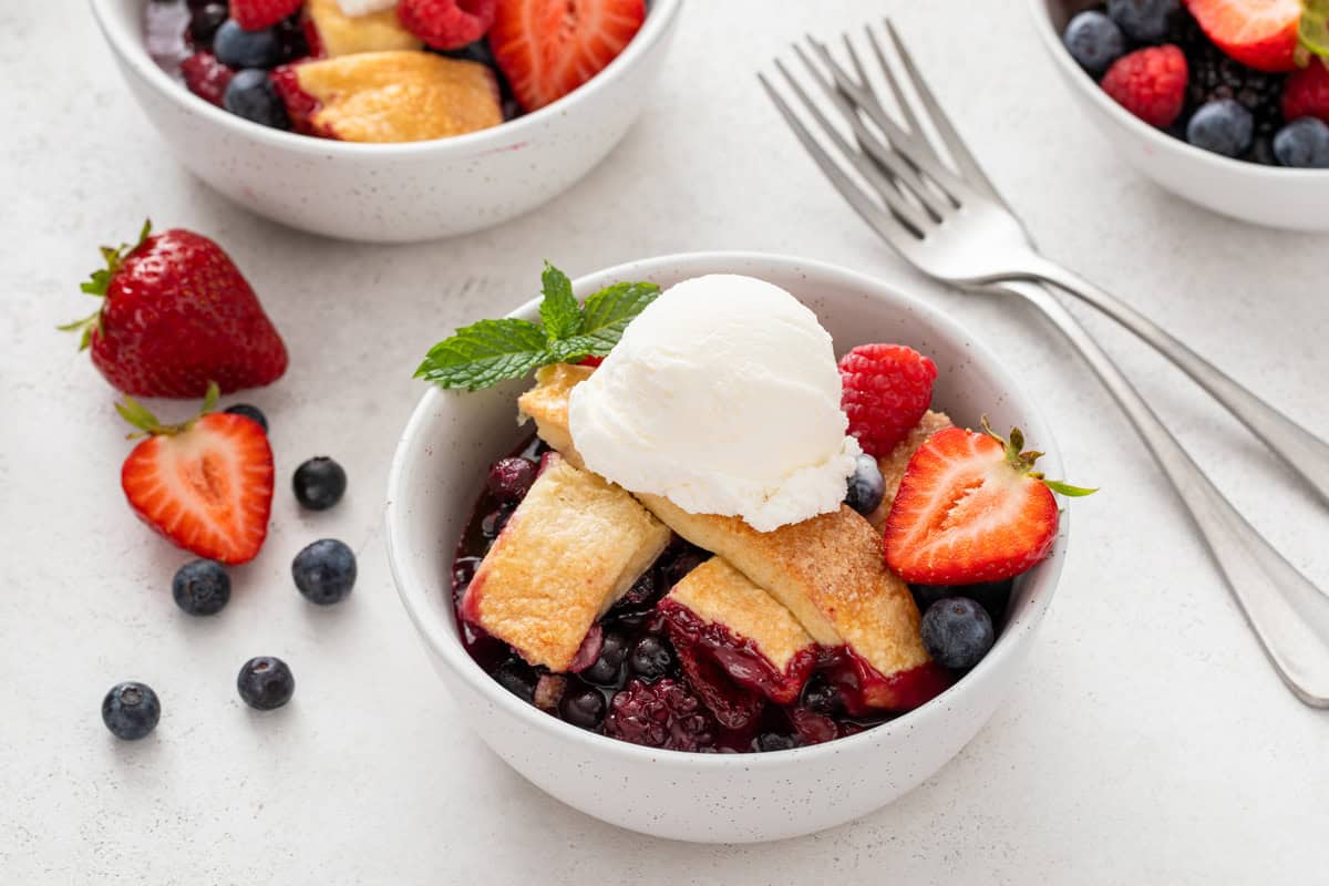 White bowl filled with mixed berry cobbler and a scoop of ice cream.