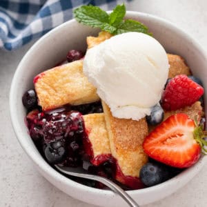 Serving of mixed berry cobbler a la mode in a white bowl.