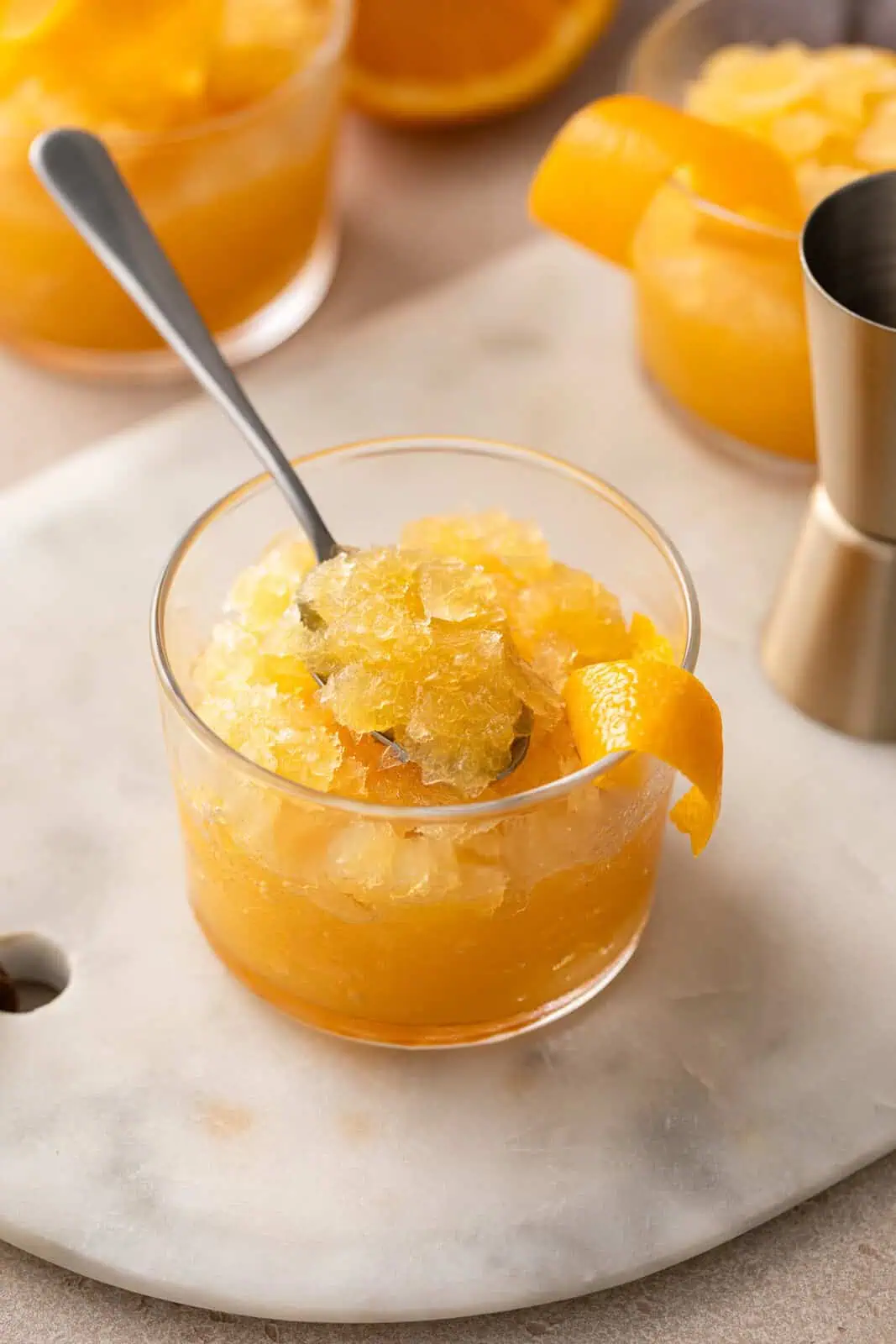 Spoon in a glass of bourbon slush garnished with an orange twist.