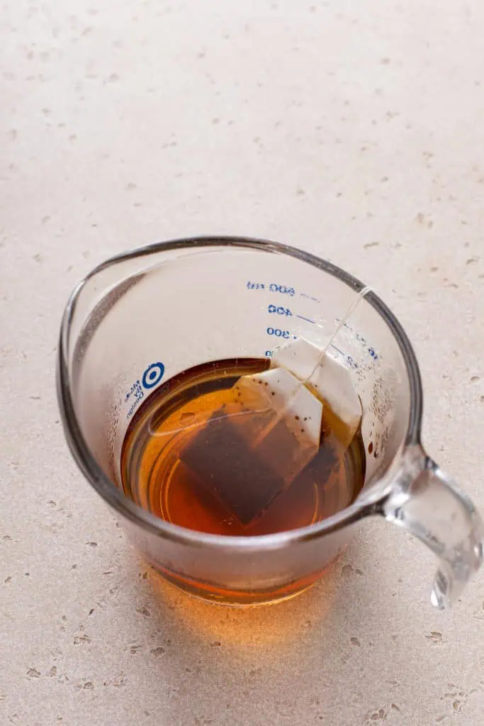 Two tea bags steeping in hot water in a measuring cup.