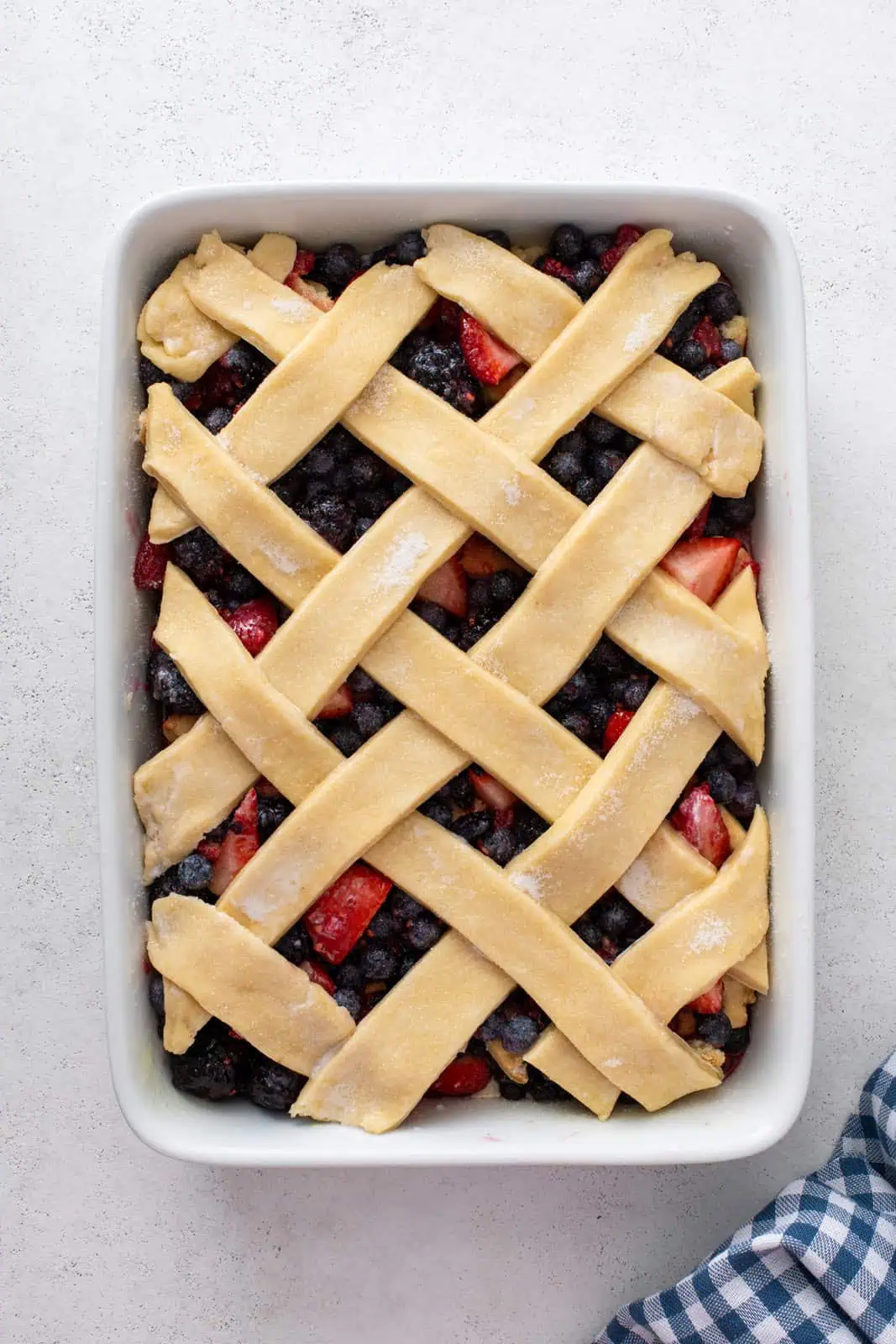 Assembled mixed berry cobbler topped with a lattice crust, ready to go in the oven.