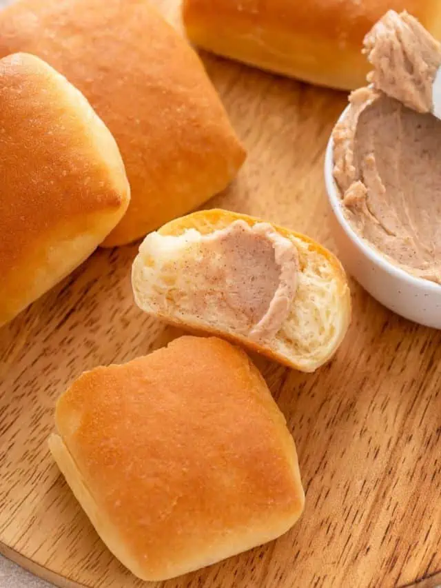 Cinnamon honey butter smeared onto a halved texas roadhouse roll on a wooden cutting board.