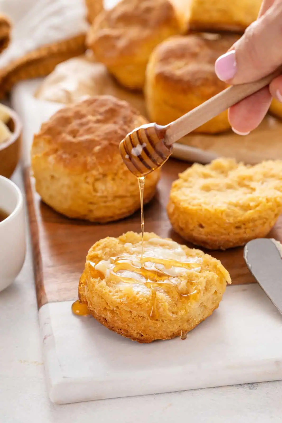 Hand drizzling honey over half of a sweet potato biscuit.