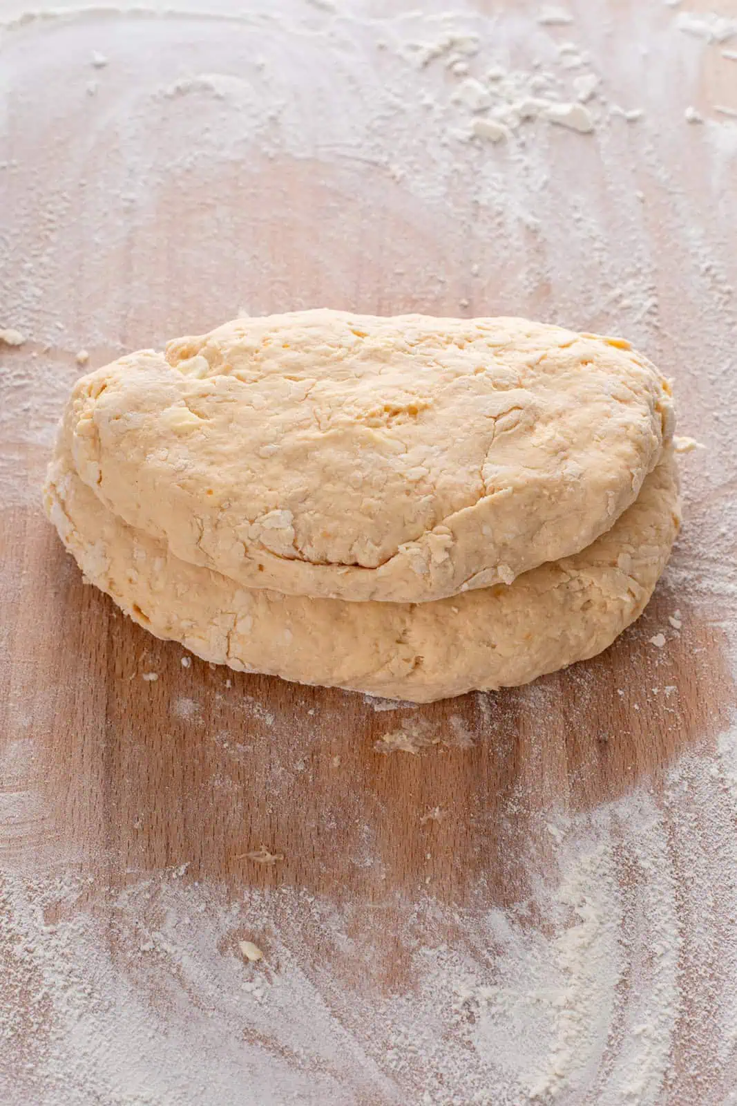 Folded disk of sweet potato biscuit dough on a floured wooden board.