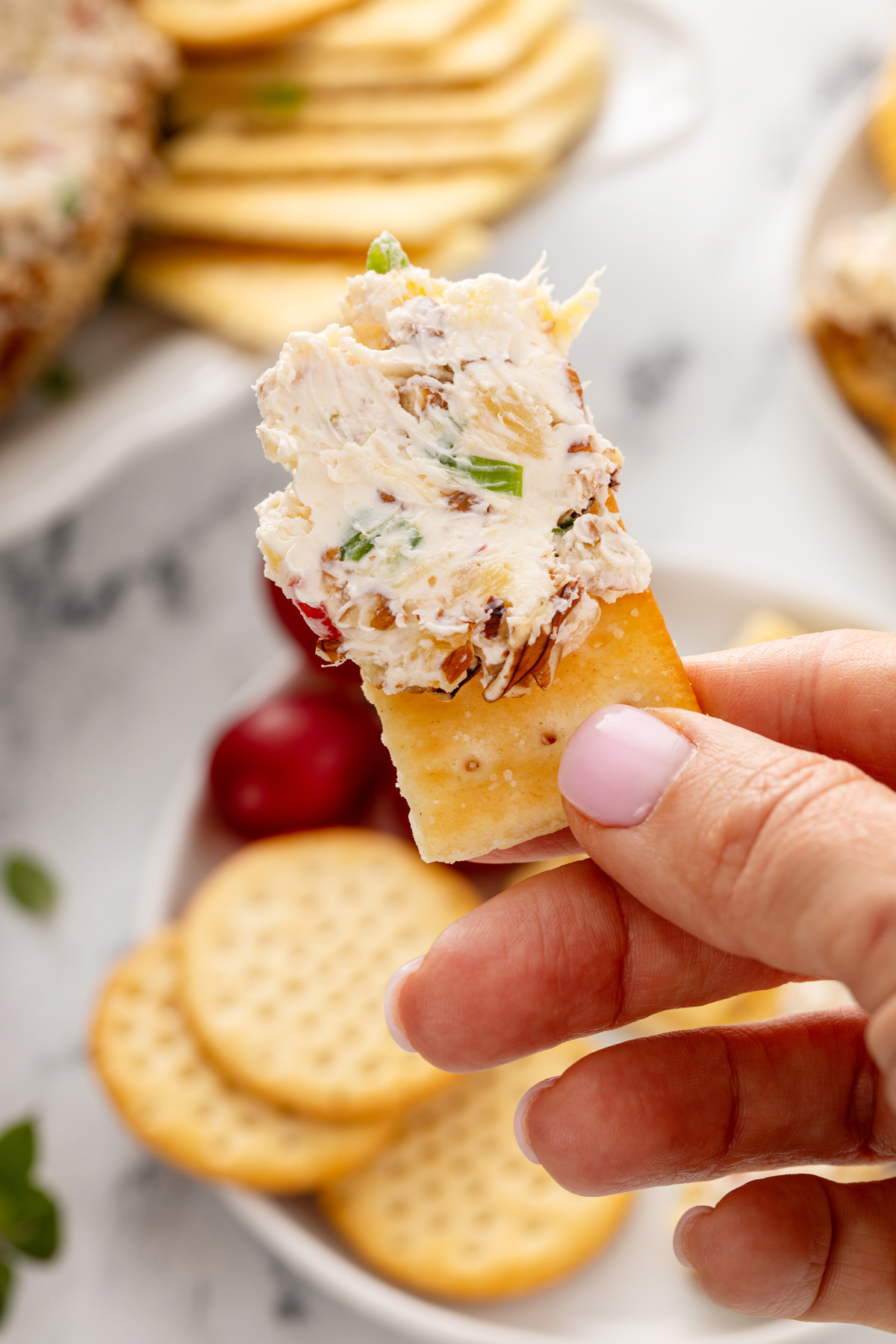 Hand holding up a cracker with a bite of pineapple cheese ball on it.