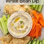 Overhead view of a platter holding pita chips, carrots, celery, and a bowl of white bean dip. Text overlay includes recipe name.