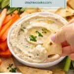 Hand dipping a pita chip into a bowl of white bean dip. Text overlay includes recipe name.