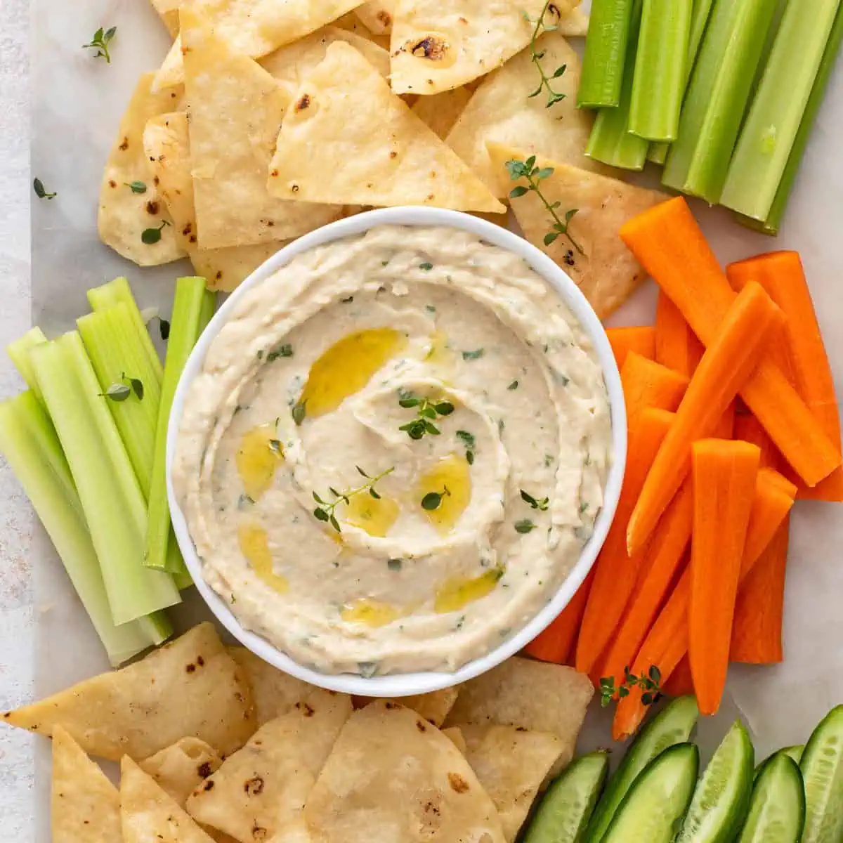 Bowl of garlic parmesan white bean dip on a platter with chips and veggies.