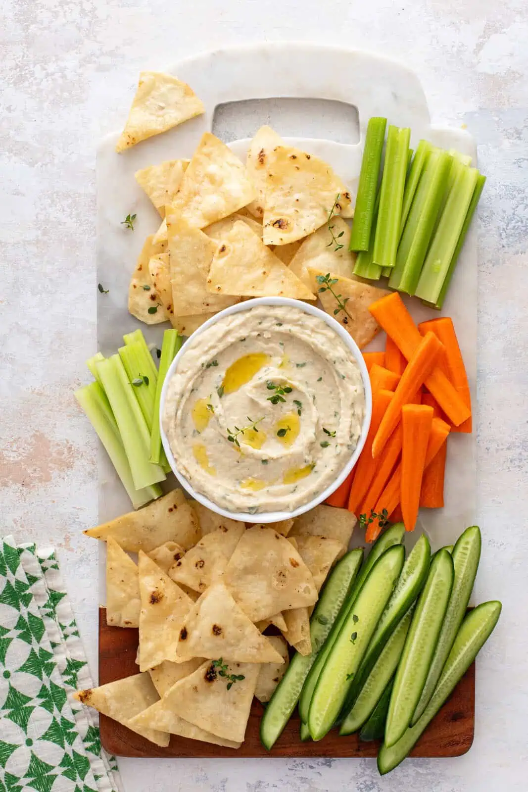 Overhead view of a platter holding pita chips, carrots, celery, and a bowl of white bean dip.