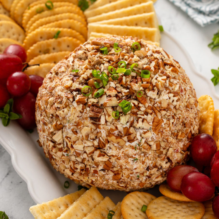 Pineapple cheese ball on a board with crackers and grapes.