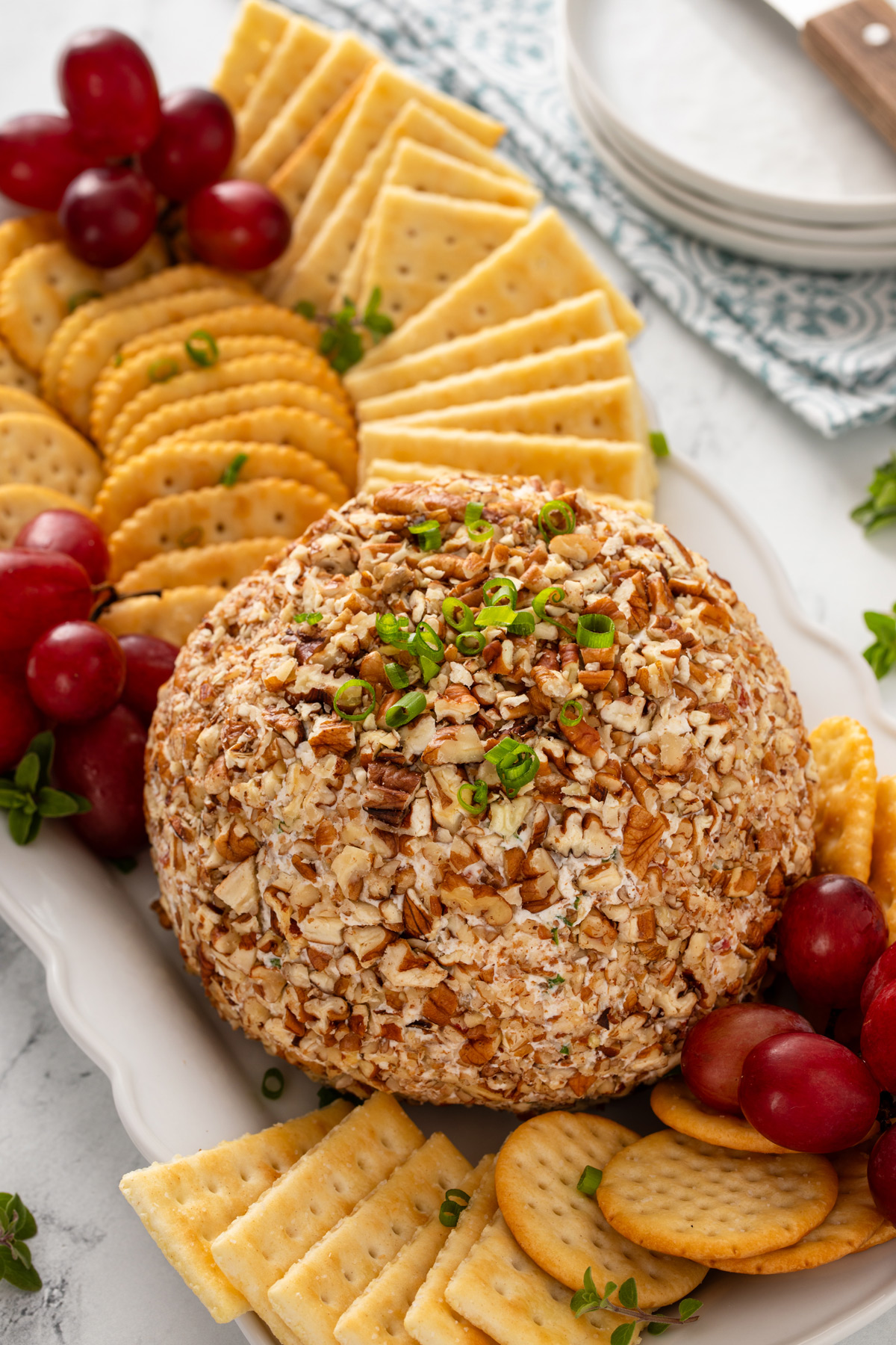 Pineapple pecan cheese ball on a white plate next to assorted crackers and grapes.