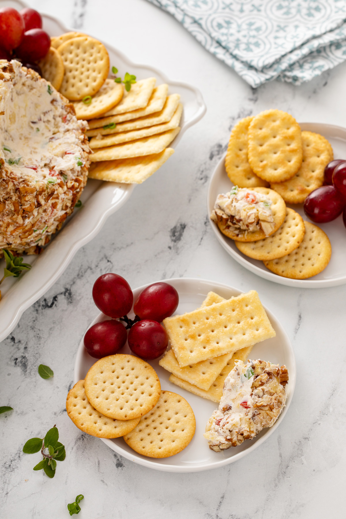 Two white plates, each holding portions of pineapple cheese ball, crackers, and grapes.