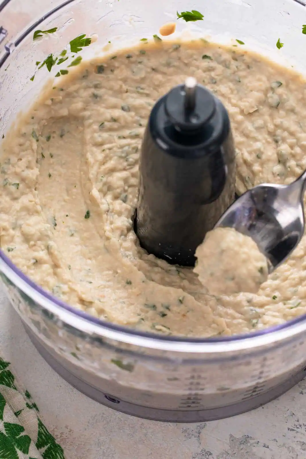 White bean dip in the bowl of a food processor, with a spoon showing the creamy consistency.