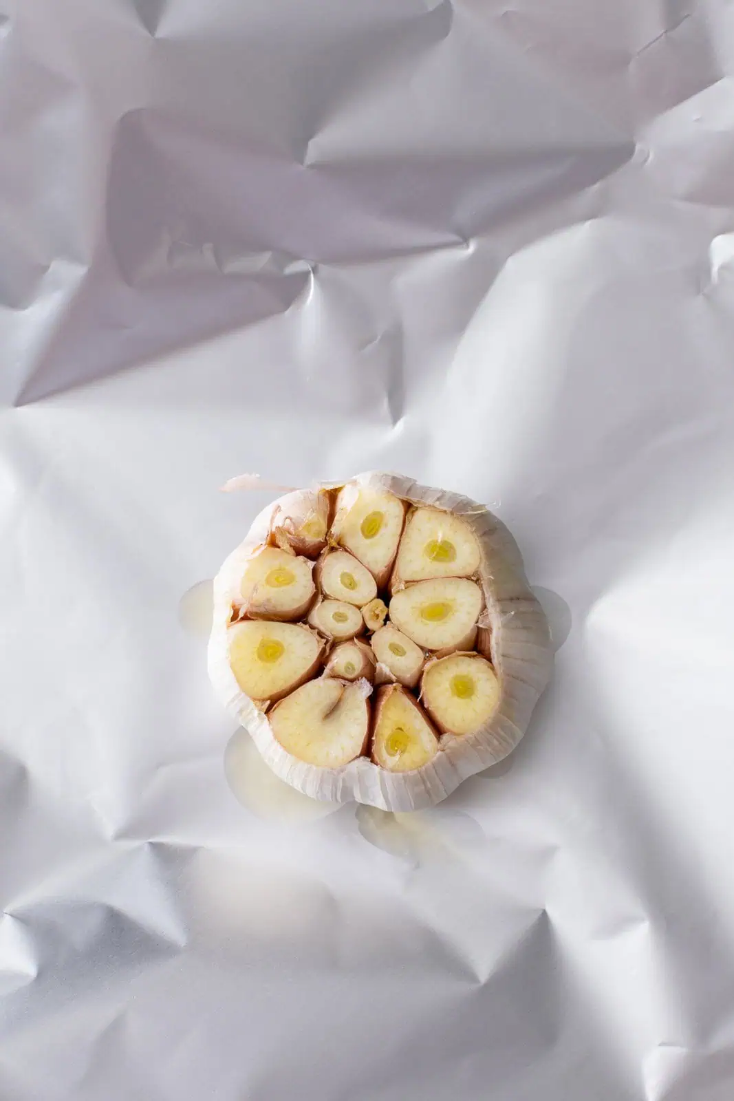 Head of garlic drizzled with olive oil on foil, ready to be roasted.