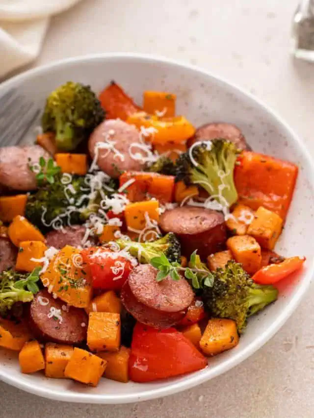 White bowl filled with sheet pan sausage and vegetables, garnished with parmesan cheese.