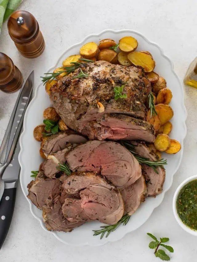 Overhead view of sliced roasted boneless leg of lamb on a platter, surrounded by roasted potatoes.